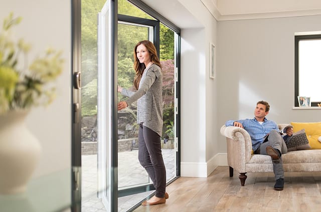 Woman opening large sliding patio doors from a modern living room to the garden
