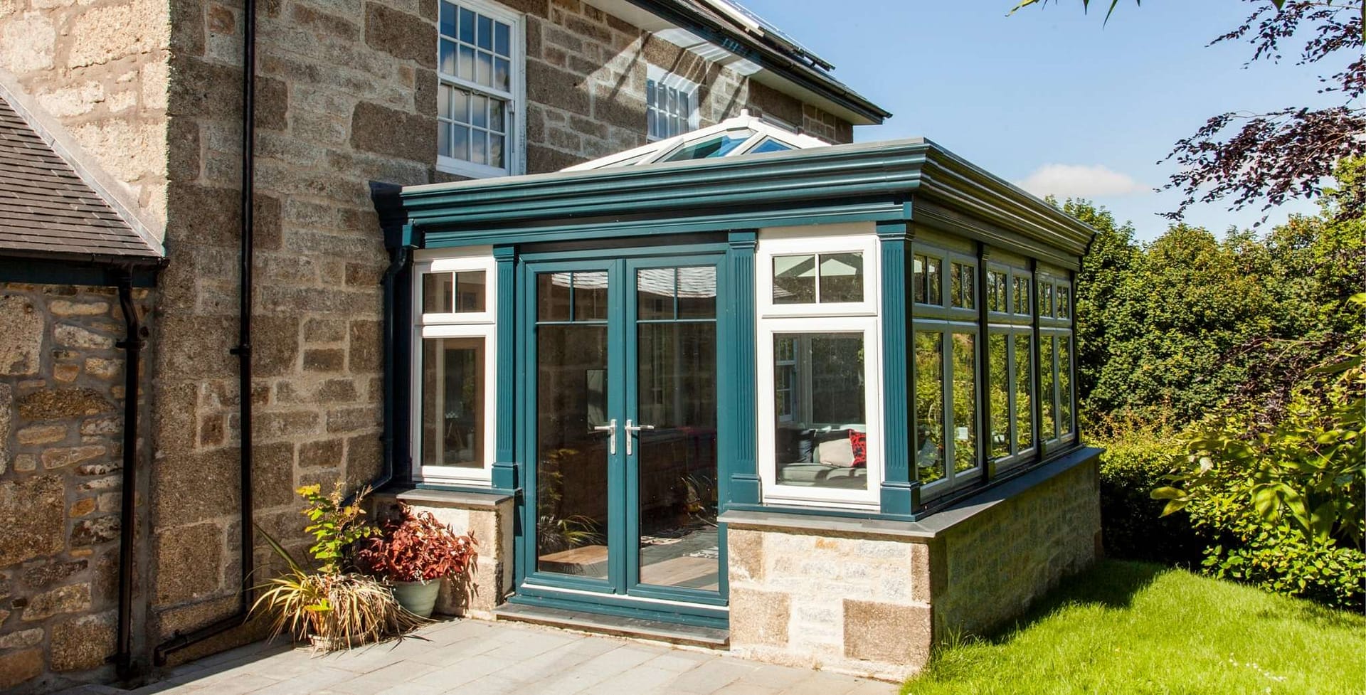 Bespoke green aluminium conservatory extension on a traditional stone house with garden views