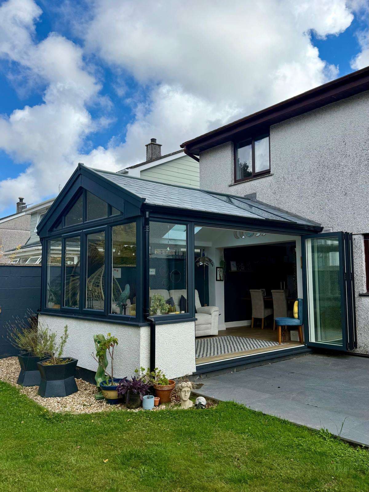 Exterior view of the transformed garden room with glazed gable and bifold doors open to the patio.